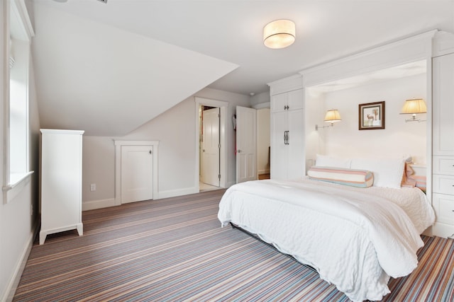 bedroom featuring dark colored carpet, connected bathroom, and vaulted ceiling