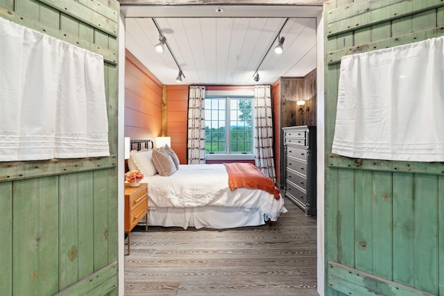 bedroom with wood walls, wood-type flooring, and track lighting