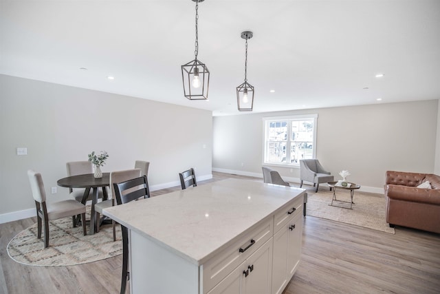 kitchen featuring light stone counters, hanging light fixtures, a kitchen island, light hardwood / wood-style floors, and white cabinets