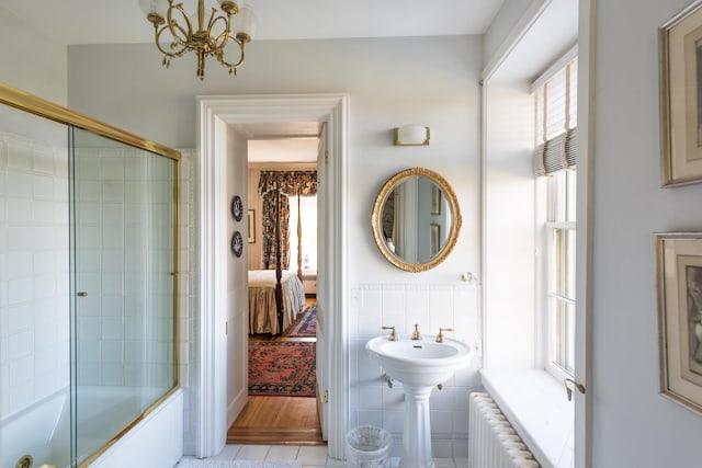 bathroom featuring bath / shower combo with glass door, radiator, and a chandelier