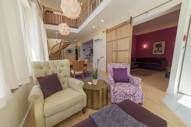 interior space with a wall mounted air conditioner, an inviting chandelier, a barn door, a towering ceiling, and light hardwood / wood-style floors