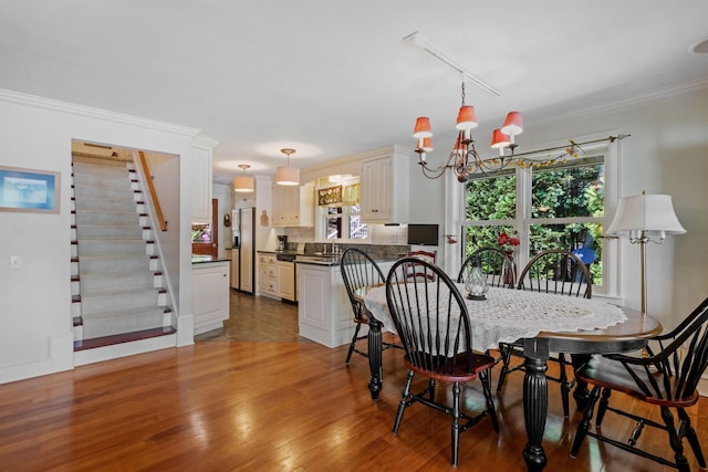 dining area with a notable chandelier, wood finished floors, ornamental molding, stairway, and rail lighting