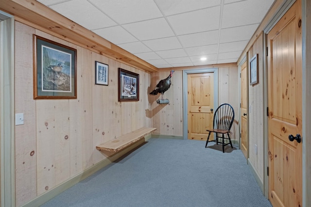 interior space with carpet flooring, wooden walls, and a drop ceiling