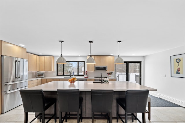 kitchen featuring pendant lighting, a kitchen island with sink, stainless steel appliances, tasteful backsplash, and light brown cabinets