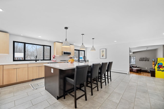 kitchen featuring pendant lighting, sink, an island with sink, a kitchen bar, and light brown cabinetry