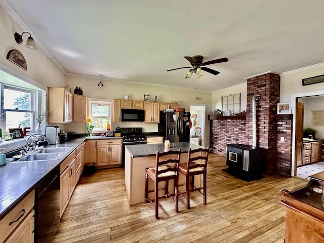 kitchen with a center island, a wood stove, black appliances, a kitchen breakfast bar, and sink