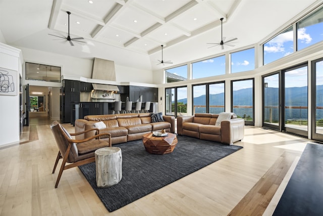 living room with beamed ceiling, light wood-type flooring, a high ceiling, and coffered ceiling