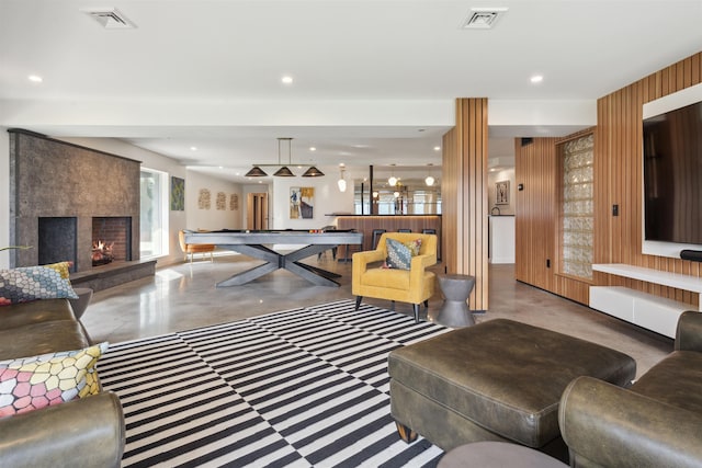 living room featuring radiator, billiards, wooden walls, concrete floors, and a large fireplace