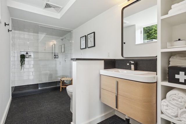 bathroom with tile patterned flooring, vanity, toilet, and tiled shower