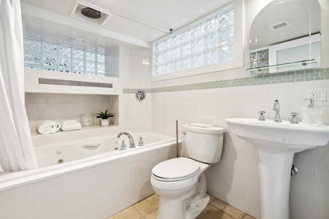 bathroom with tile patterned flooring, a relaxing tiled tub, toilet, and tile walls