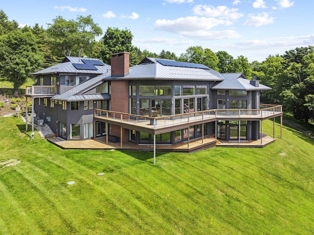 rear view of house with solar panels, a deck, cooling unit, and a lawn