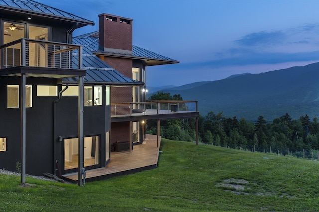 back house at dusk with a mountain view, a balcony, and a yard