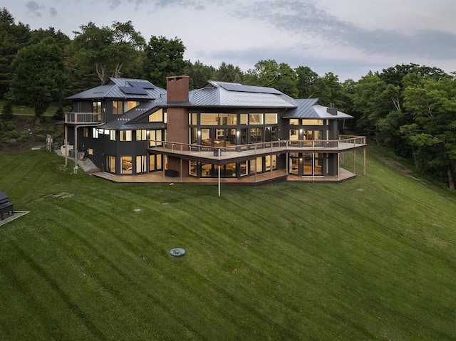 back of property with a lawn, a deck, and solar panels