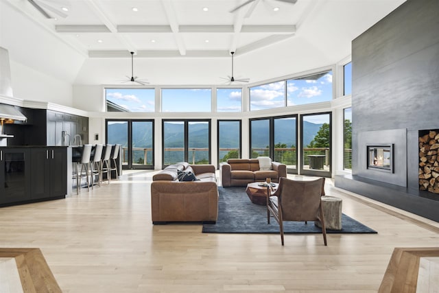 living room featuring beam ceiling, light hardwood / wood-style flooring, a mountain view, a high ceiling, and plenty of natural light