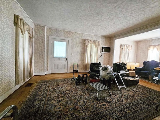 living room featuring wallpapered walls, visible vents, wood finished floors, a wood stove, and a textured ceiling