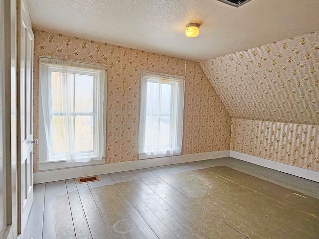 additional living space featuring visible vents, a textured ceiling, hardwood / wood-style floors, and wallpapered walls