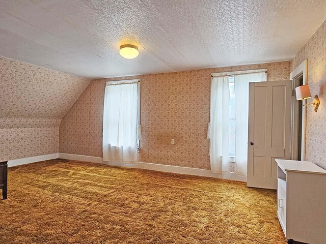 bonus room with light colored carpet, a textured ceiling, baseboards, and wallpapered walls