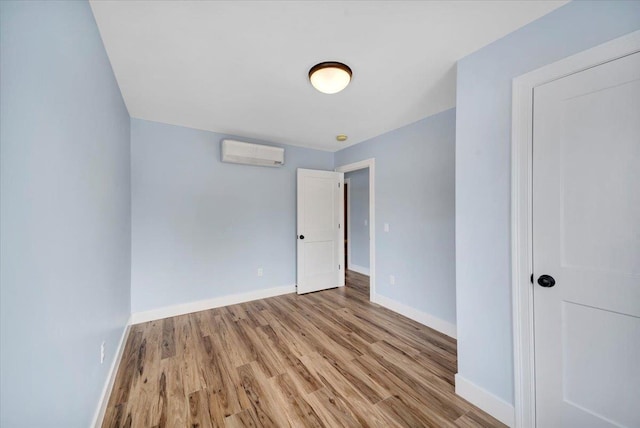 spare room with a wall unit AC, baseboards, and wood finished floors