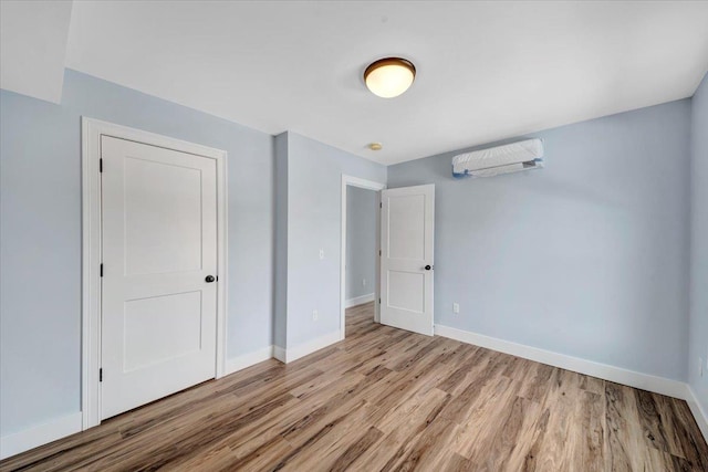 unfurnished bedroom with baseboards, light wood-style floors, and a wall unit AC