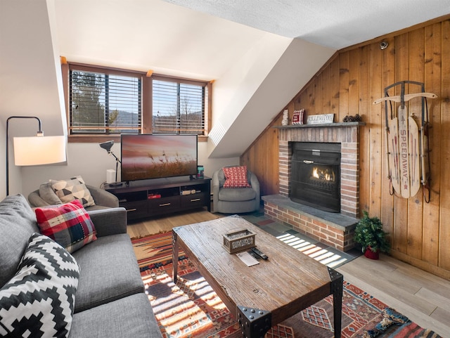 living room featuring vaulted ceiling, a fireplace, wooden walls, light wood-type flooring, and a textured ceiling