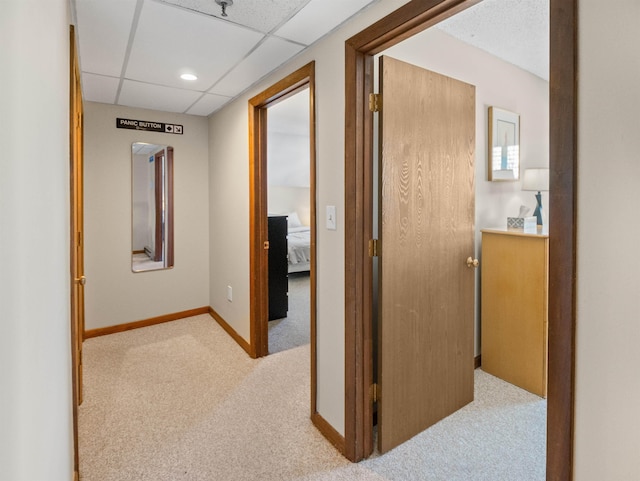 hall with light carpet and a paneled ceiling