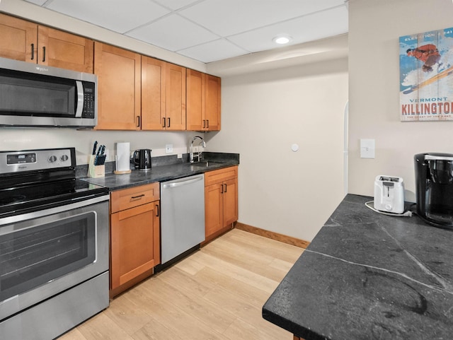 kitchen with a paneled ceiling, sink, stainless steel appliances, and light hardwood / wood-style flooring