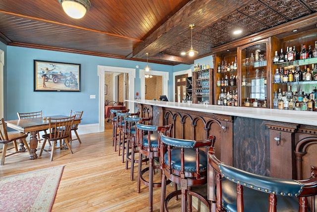 bar featuring crown molding, light hardwood / wood-style flooring, decorative light fixtures, wooden ceiling, and beamed ceiling