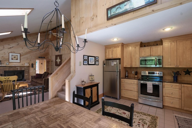 kitchen featuring light brown cabinetry, a brick fireplace, light tile patterned floors, wooden walls, and stainless steel appliances