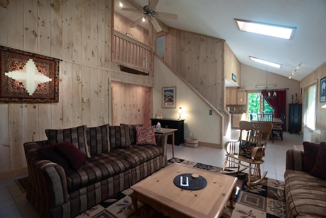 living room featuring high vaulted ceiling, wooden walls, rail lighting, light tile patterned floors, and ceiling fan