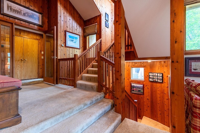 staircase with carpet flooring, wood walls, and vaulted ceiling