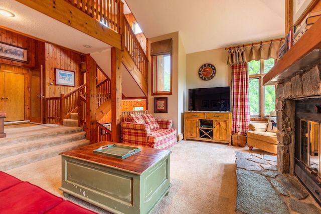 carpeted living room with a stone fireplace, wooden walls, and a high ceiling