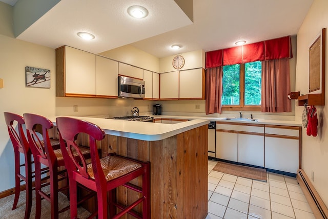 kitchen featuring white cabinets, sink, a baseboard radiator, a kitchen bar, and kitchen peninsula