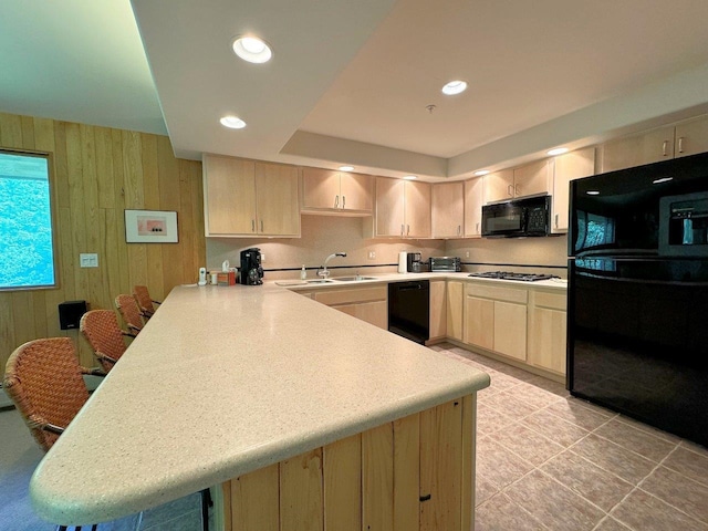 kitchen with light brown cabinetry, wooden walls, black appliances, sink, and kitchen peninsula