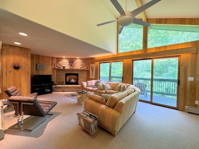 carpeted living room featuring a stone fireplace, high vaulted ceiling, baseboard heating, wooden walls, and ceiling fan