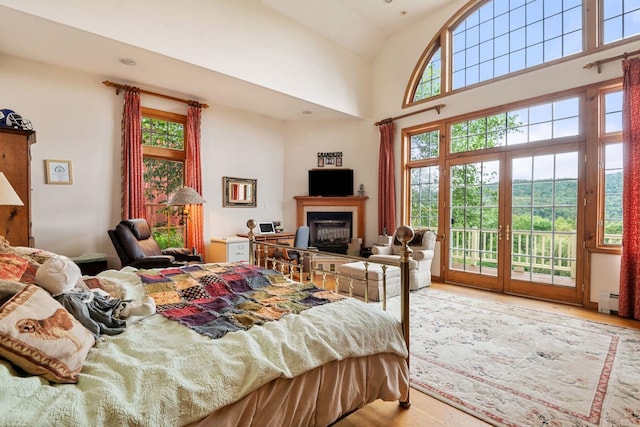 bedroom with light hardwood / wood-style floors, access to exterior, baseboard heating, and high vaulted ceiling