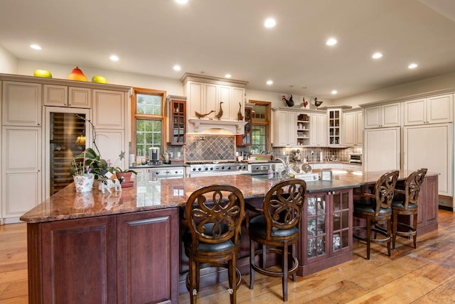 kitchen with a large island with sink, light hardwood / wood-style flooring, dark stone counters, and a breakfast bar area