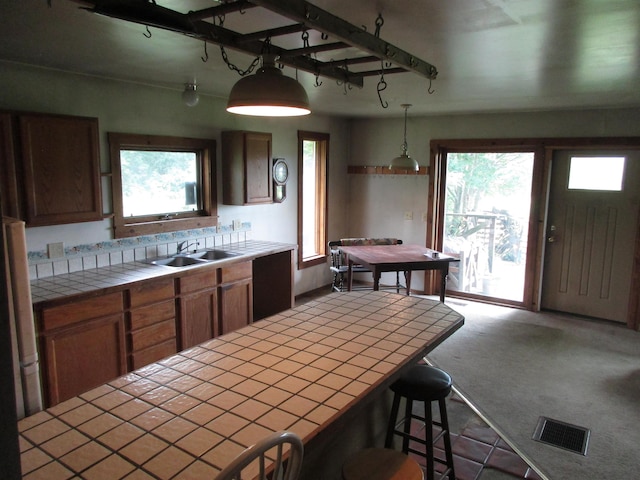 kitchen featuring decorative light fixtures, visible vents, a sink, tile counters, and carpet