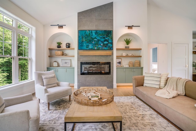 living room featuring a tile fireplace, vaulted ceiling, light hardwood / wood-style floors, and built in shelves