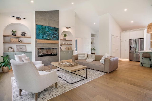 living room featuring built in shelves, high vaulted ceiling, a tile fireplace, and light hardwood / wood-style flooring