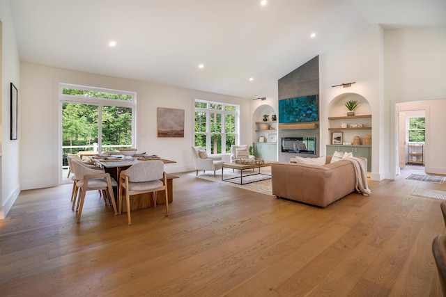 living room with built in shelves, high vaulted ceiling, a fireplace, and light hardwood / wood-style floors