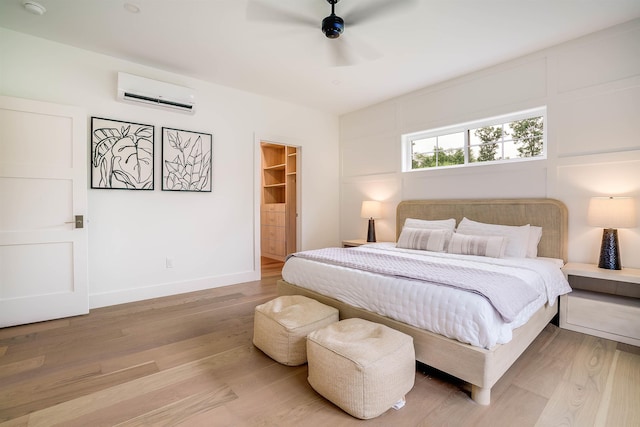 bedroom with wood-type flooring, a spacious closet, a closet, a wall unit AC, and ceiling fan