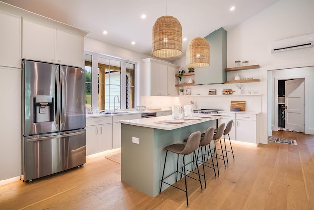 kitchen featuring stainless steel refrigerator with ice dispenser, a breakfast bar, white cabinetry, a wall mounted air conditioner, and hanging light fixtures