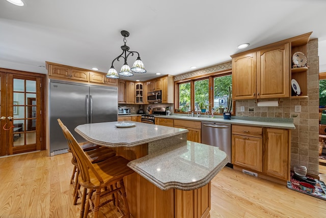 kitchen with stainless steel appliances, a kitchen island, light wood-style floors, decorative backsplash, and glass insert cabinets