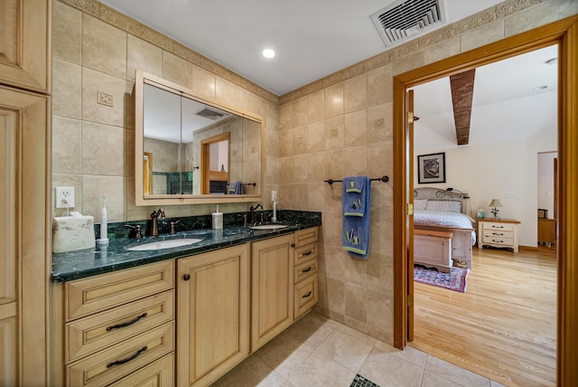 ensuite bathroom with a sink, visible vents, and tile walls