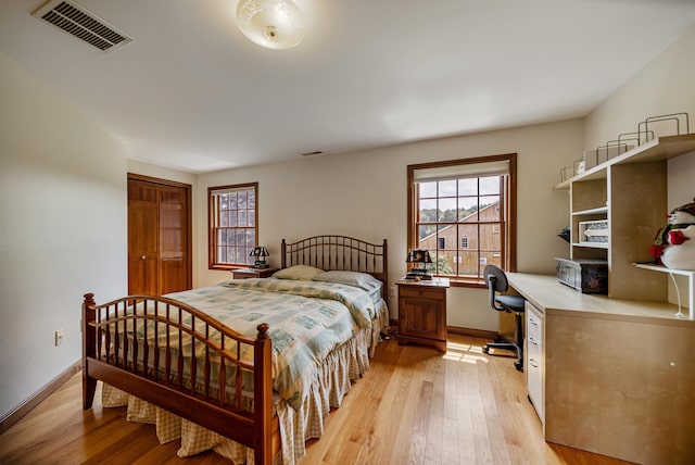 bedroom featuring light wood finished floors, built in desk, visible vents, and baseboards