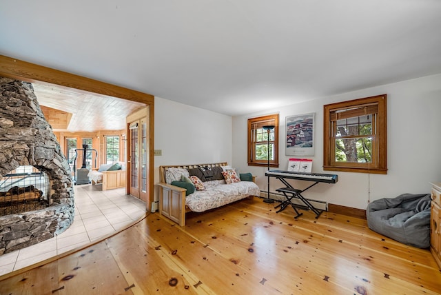 living room featuring a baseboard heating unit, vaulted ceiling, a stone fireplace, and hardwood / wood-style floors