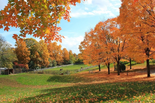 view of community with fence, a lawn, and a rural view