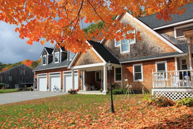 view of front of house featuring aphalt driveway, roof with shingles, covered porch, an attached garage, and a front yard