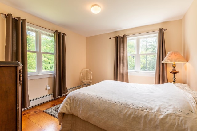 bedroom with multiple windows, hardwood / wood-style floors, and a baseboard heating unit