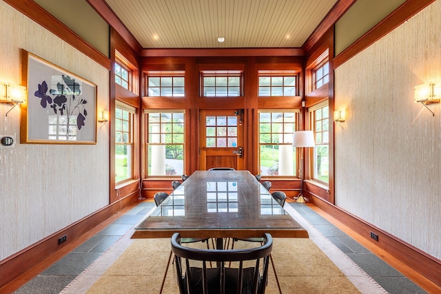 dining space featuring a towering ceiling, plenty of natural light, and wooden walls